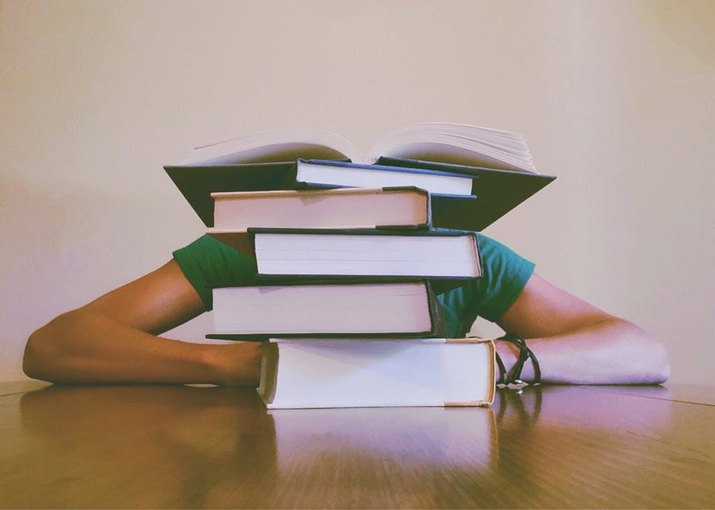A student hidden behind a stack of books, symbolizing academic stress and study challenges.