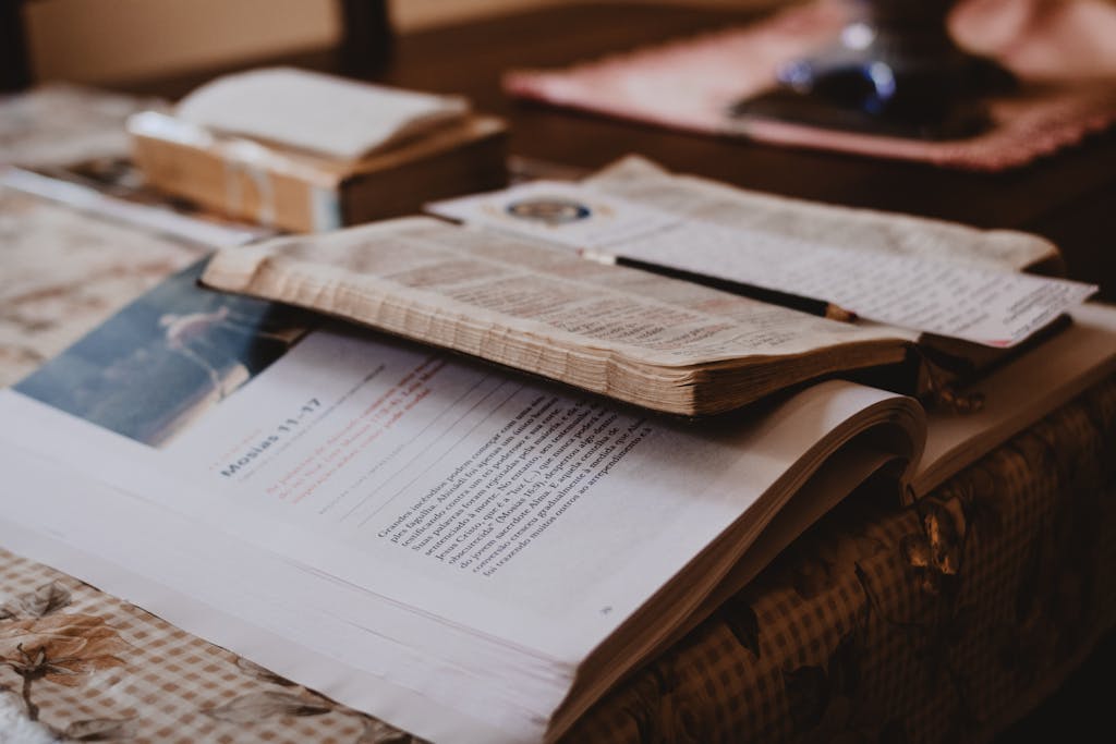 Open Bible and notebook on a wooden table with notes and a bookmark, warm lighting.