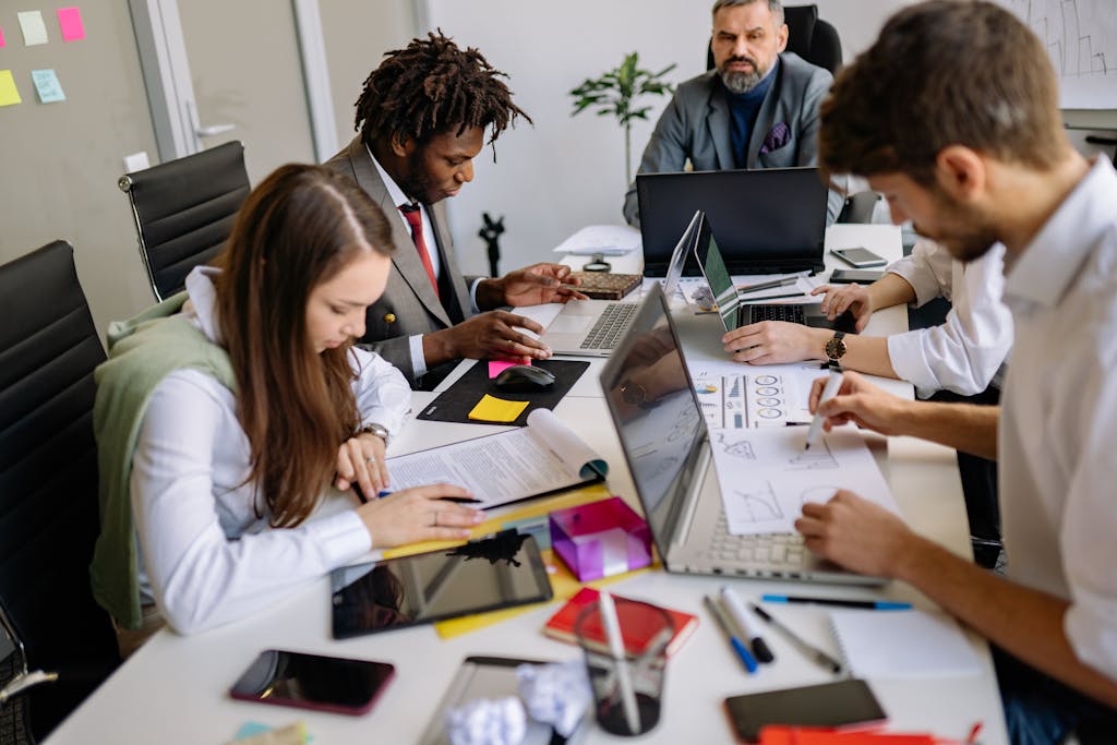 Team of professionals collaborating around a table in a modern office, focusing on projects and discussions.