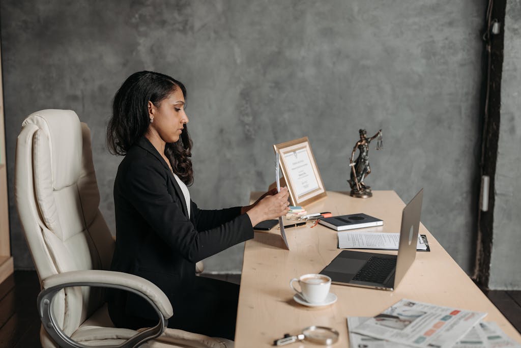 A focused businesswoman in formal attire works at her desk in a contemporary office setting.
