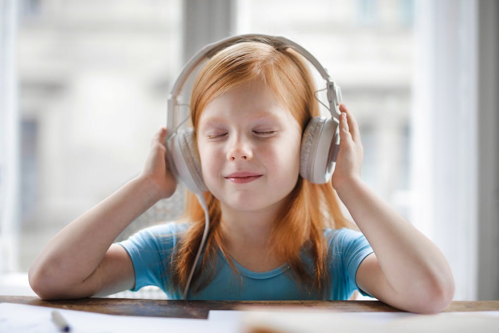 A young girl with headphones enjoying music indoors with a joyful expression.