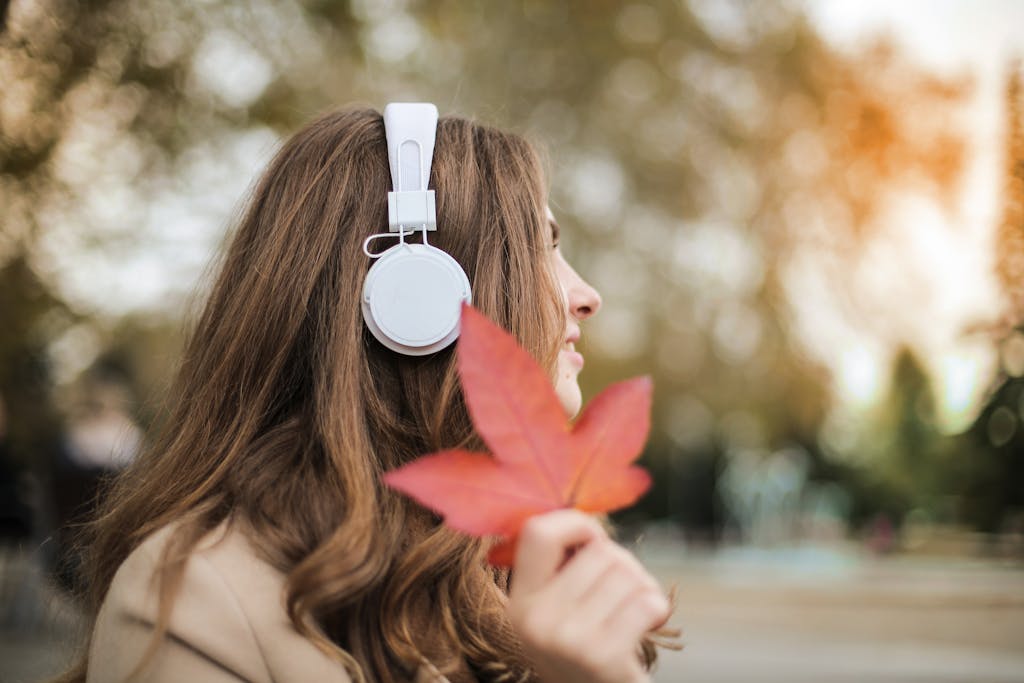 Woman with headphones enjoys music outdoors holding a maple leaf.