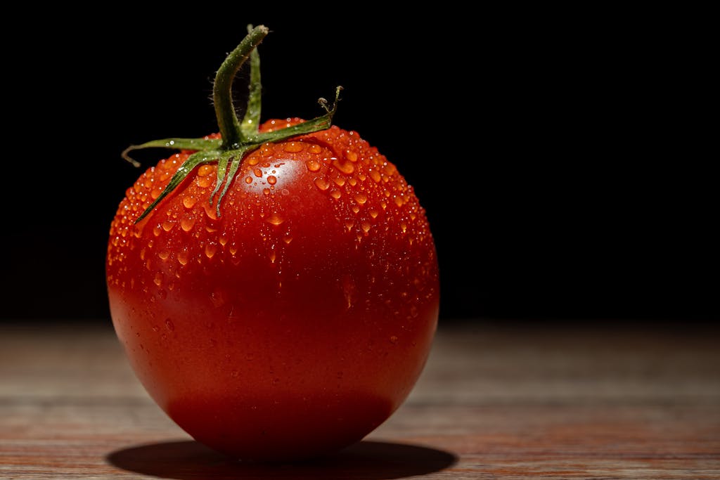 Close-up of a ripe, fresh tomato with water droplets on a wooden surface.